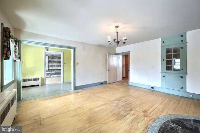 empty room with light hardwood / wood-style flooring, radiator heating unit, and a chandelier