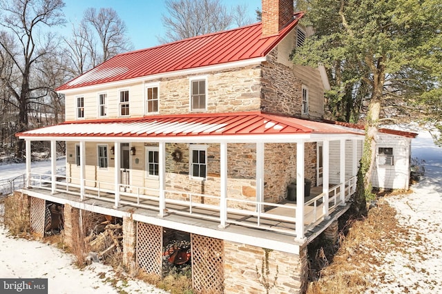 snow covered house featuring a sunroom and covered porch