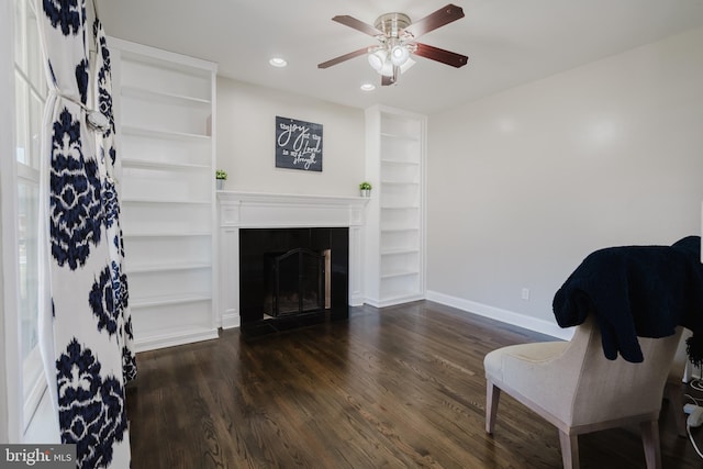 sitting room with dark wood-type flooring, ceiling fan, and built in features