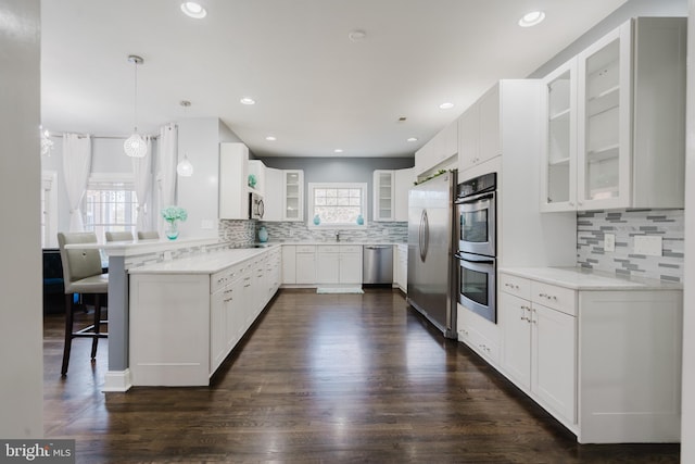 kitchen with appliances with stainless steel finishes, a breakfast bar, white cabinetry, hanging light fixtures, and dark wood-type flooring