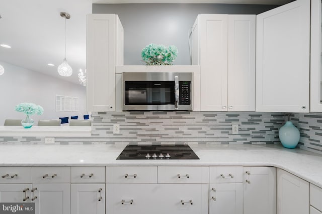 kitchen featuring pendant lighting, tasteful backsplash, white cabinets, light stone counters, and black electric cooktop