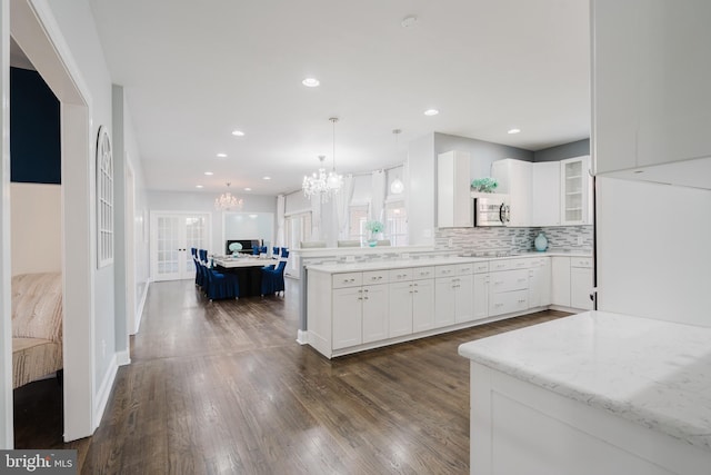 kitchen featuring pendant lighting, white cabinetry, light stone countertops, dark wood-type flooring, and an inviting chandelier