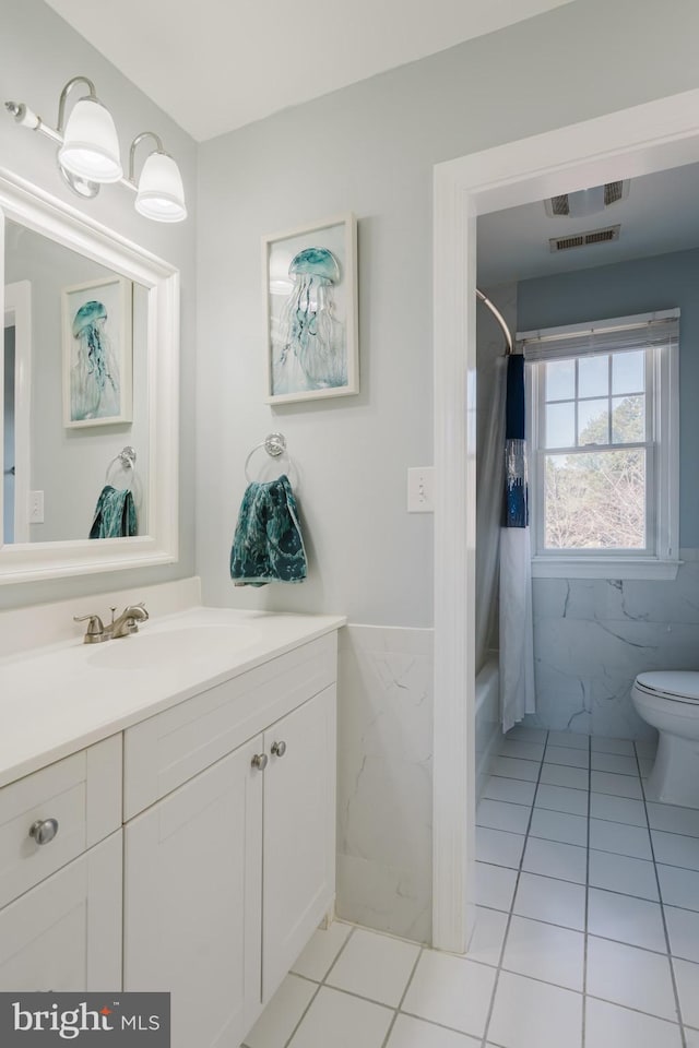 full bathroom with shower / tub combo with curtain, tile walls, vanity, tile patterned floors, and toilet