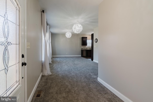 hallway with a notable chandelier and dark colored carpet