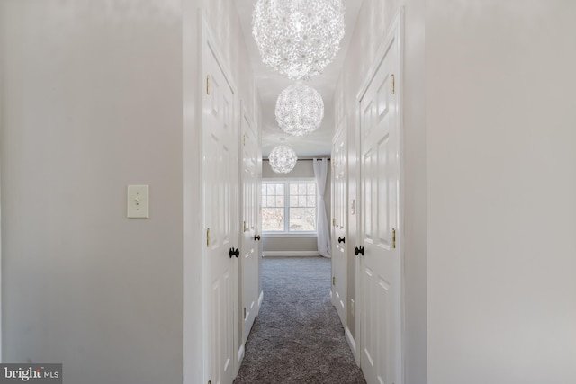 hallway featuring a notable chandelier and dark colored carpet