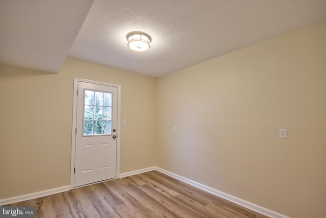 doorway to outside with a textured ceiling and light hardwood / wood-style floors