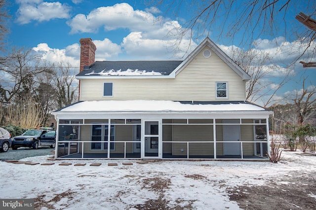 snow covered back of property with a sunroom