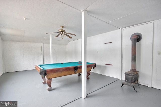 rec room with billiards, concrete flooring, ceiling fan, and a wood stove