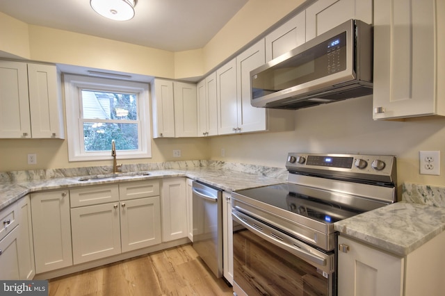 kitchen featuring sink, white cabinets, light stone counters, light hardwood / wood-style floors, and stainless steel appliances