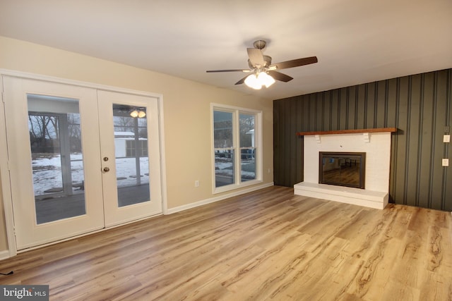 unfurnished living room featuring wood-type flooring, ceiling fan, a fireplace, and french doors