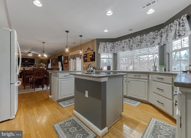 kitchen with kitchen peninsula, light hardwood / wood-style flooring, hanging light fixtures, white refrigerator, and a kitchen island