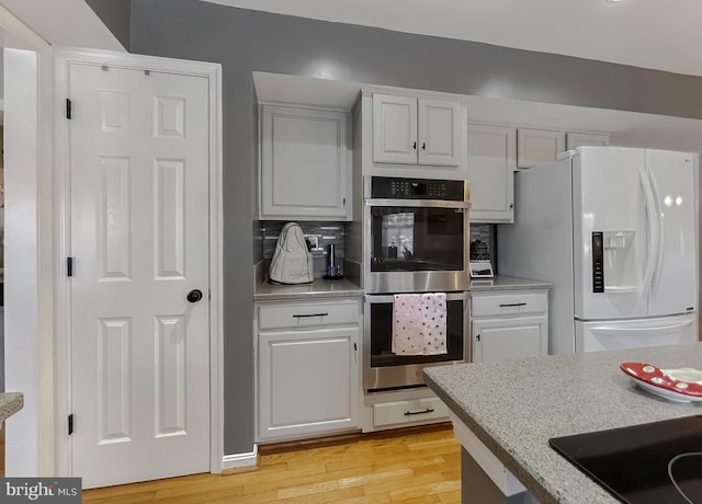 kitchen featuring white refrigerator with ice dispenser, double oven, tasteful backsplash, black electric cooktop, and light hardwood / wood-style floors