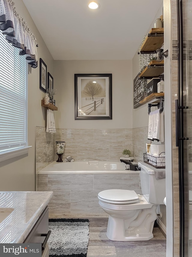 bathroom with hardwood / wood-style floors, toilet, a relaxing tiled tub, and vanity