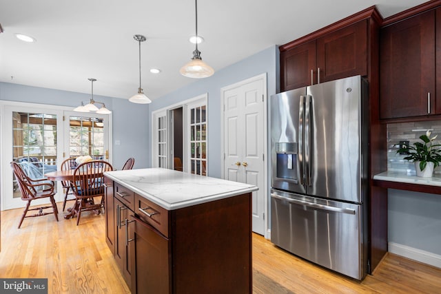 kitchen with stainless steel fridge, a center island, light stone countertops, decorative backsplash, and decorative light fixtures