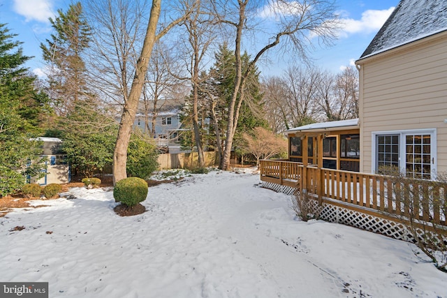 yard layered in snow with a wooden deck and a sunroom