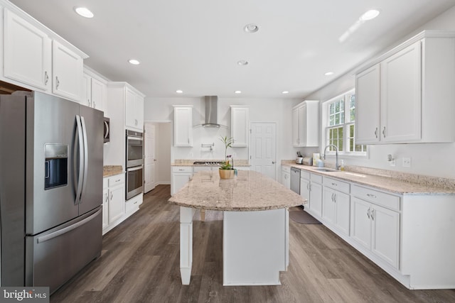 kitchen featuring wall chimney exhaust hood, sink, white cabinets, a center island, and stainless steel appliances