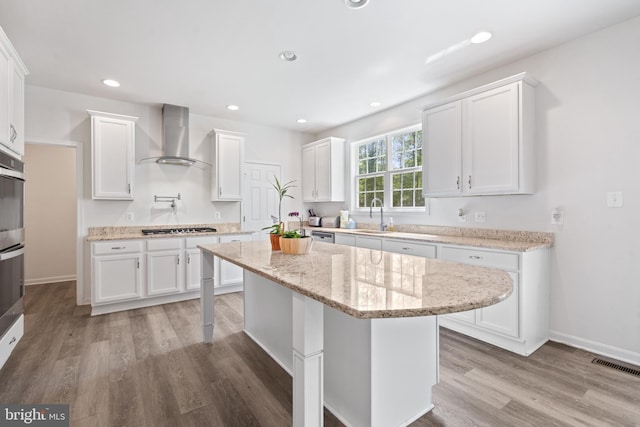 kitchen featuring wall chimney range hood, white cabinets, a center island, and appliances with stainless steel finishes