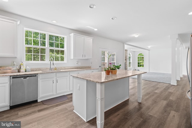 kitchen with light stone countertops, a center island, white cabinetry, sink, and stainless steel dishwasher