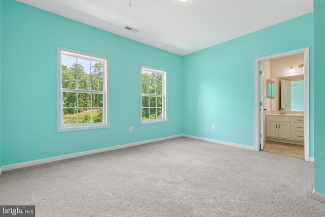 unfurnished bedroom featuring ensuite bathroom and light carpet