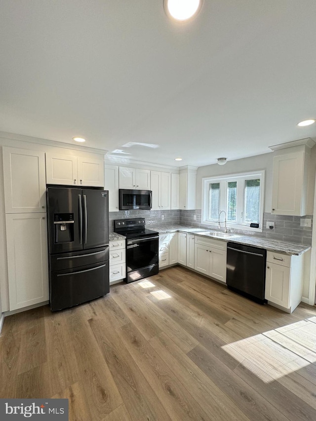 kitchen with white cabinets, black appliances, sink, light wood-type flooring, and light stone counters