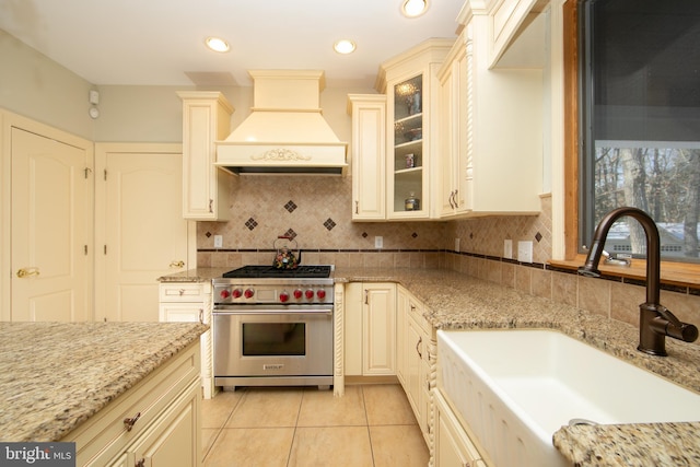 kitchen with premium stove, sink, light stone counters, and premium range hood