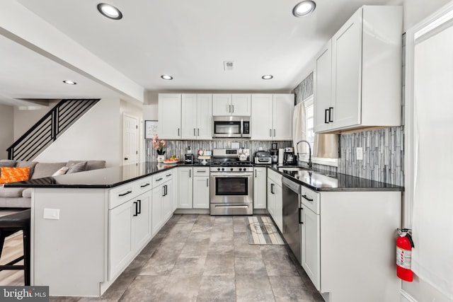 kitchen with a breakfast bar, kitchen peninsula, sink, white cabinetry, and appliances with stainless steel finishes