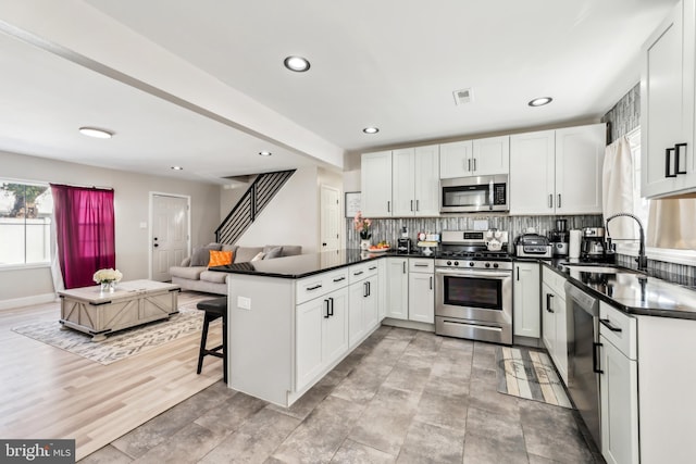 kitchen with white cabinets, stainless steel appliances, sink, a kitchen breakfast bar, and kitchen peninsula