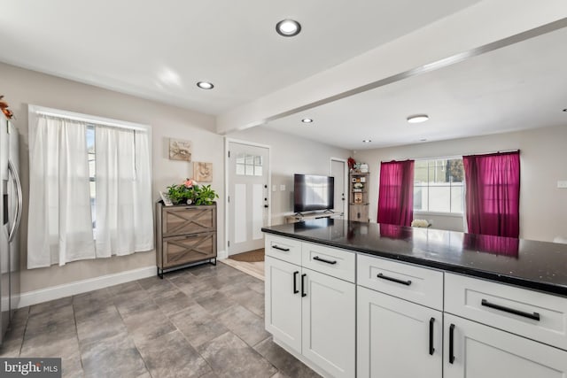 kitchen with stainless steel refrigerator with ice dispenser, beam ceiling, and white cabinets