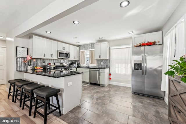 kitchen featuring kitchen peninsula, stainless steel appliances, white cabinets, and a breakfast bar