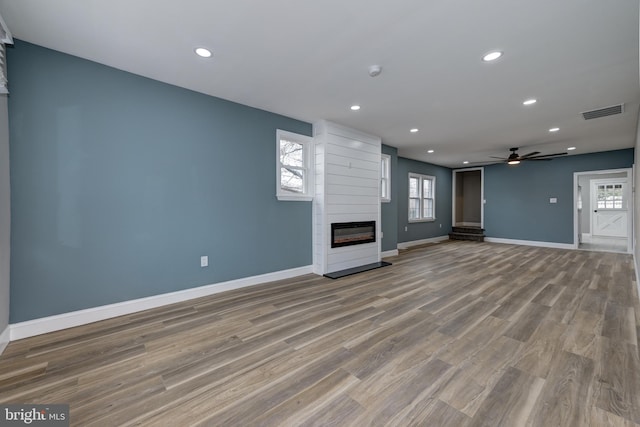 unfurnished living room with light hardwood / wood-style floors, a large fireplace, and ceiling fan