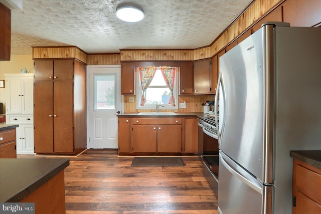 kitchen with appliances with stainless steel finishes, sink, a textured ceiling, and dark hardwood / wood-style floors