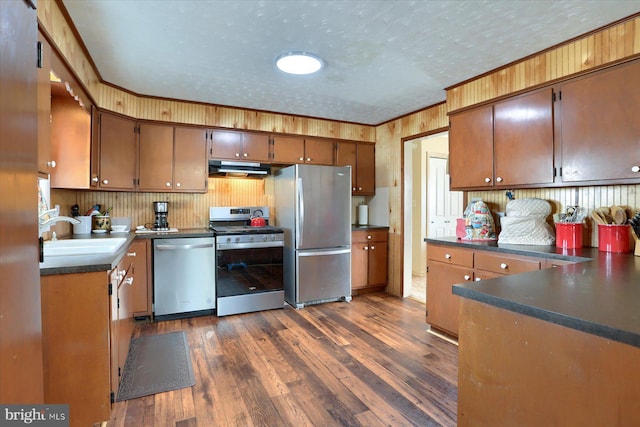 kitchen featuring sink, a textured ceiling, ornamental molding, appliances with stainless steel finishes, and dark hardwood / wood-style flooring