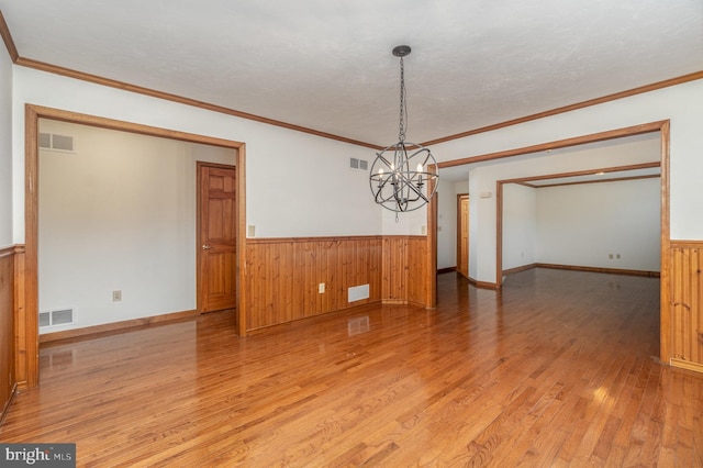 empty room with a textured ceiling, a chandelier, crown molding, and wood-type flooring