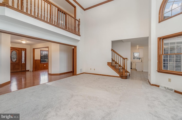 unfurnished living room with a high ceiling, crown molding, and carpet flooring