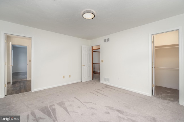 unfurnished bedroom with a spacious closet, light colored carpet, and a closet