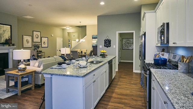 kitchen with appliances with stainless steel finishes, an island with sink, light stone counters, and white cabinetry