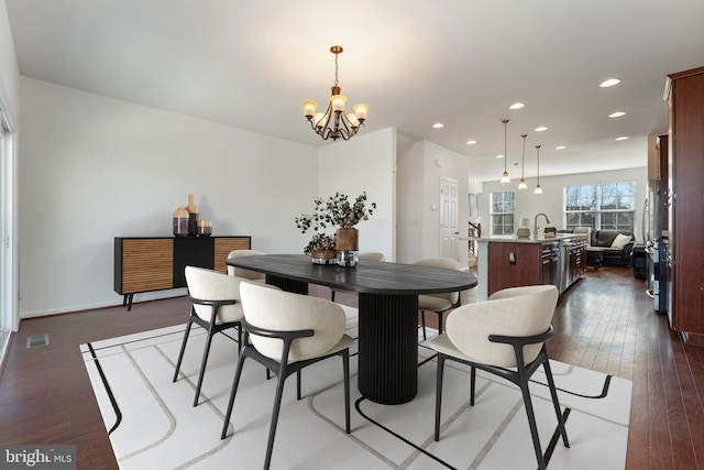 dining space with sink, a chandelier, and dark wood-type flooring