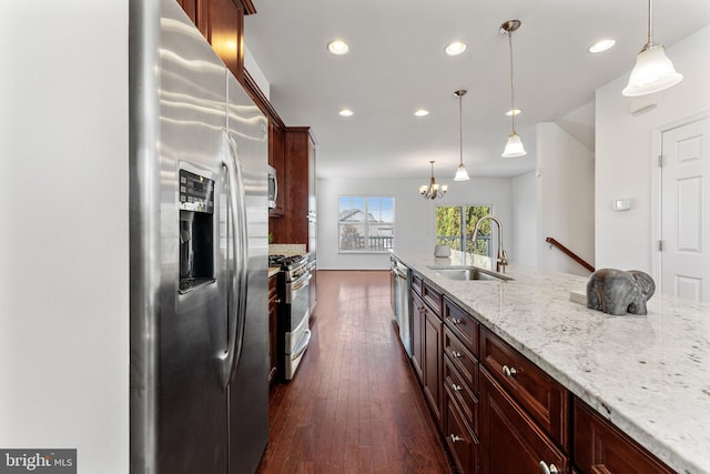 kitchen with hanging light fixtures, sink, stainless steel appliances, light stone counters, and dark hardwood / wood-style floors