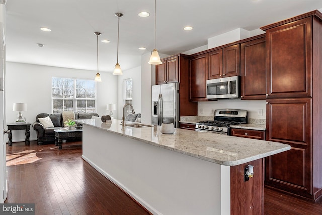 kitchen featuring appliances with stainless steel finishes, decorative light fixtures, sink, light stone counters, and a center island with sink