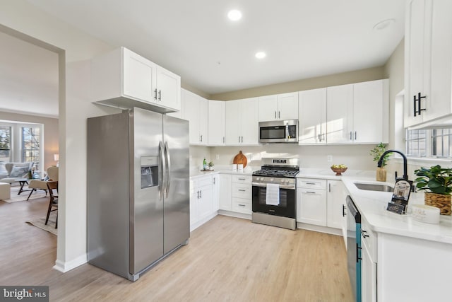 kitchen featuring sink, appliances with stainless steel finishes, white cabinetry, light hardwood / wood-style floors, and light stone countertops