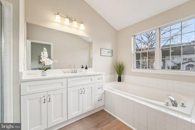 bathroom with vanity, vaulted ceiling, hardwood / wood-style floors, and tiled bath