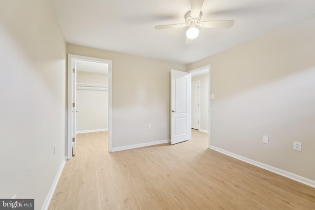 unfurnished bedroom with ceiling fan, a walk in closet, a closet, and light hardwood / wood-style flooring