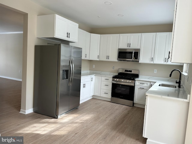 kitchen with appliances with stainless steel finishes, white cabinetry, sink, light stone counters, and light hardwood / wood-style floors