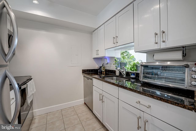 kitchen featuring appliances with stainless steel finishes, white cabinetry, a sink, and dark stone countertops