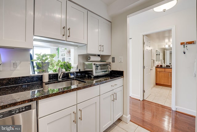 kitchen featuring a toaster, dishwasher, dark stone countertops, white cabinetry, and a sink