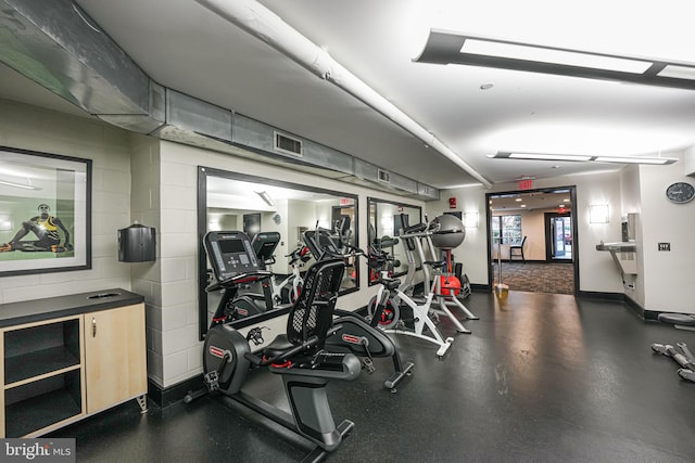 exercise room featuring concrete block wall, visible vents, and baseboards