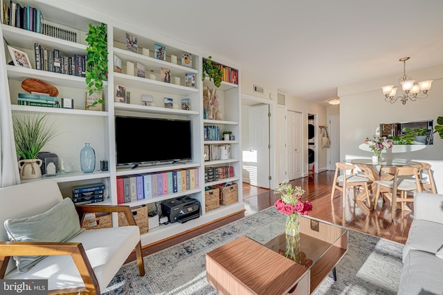 living room with a chandelier, stacked washer / drying machine, visible vents, and wood finished floors