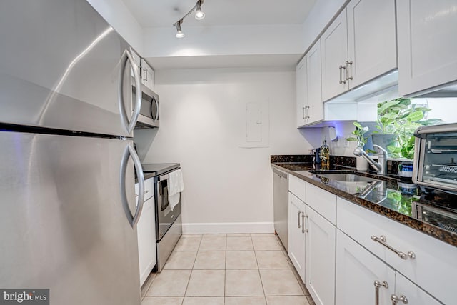 kitchen featuring light tile patterned floors, a sink, white cabinetry, appliances with stainless steel finishes, and dark stone counters