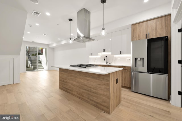 kitchen with island exhaust hood, hanging light fixtures, light wood-type flooring, appliances with stainless steel finishes, and white cabinets