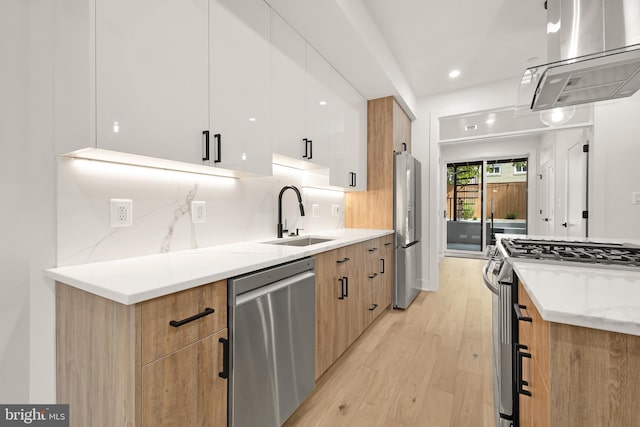 kitchen featuring light stone countertops, white cabinetry, stainless steel appliances, sink, and light wood-type flooring